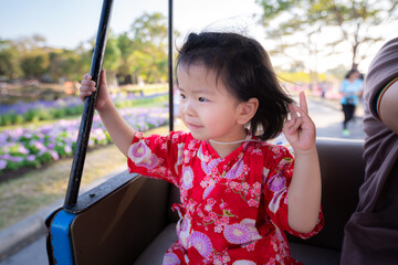 Head shot Happy girl sat with sweet smile on a rickshaw in park. Child in a traditional red...
