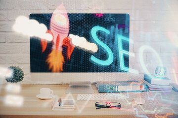 Double exposure of table with computer and seo drawing hologram. Search optimization concept.