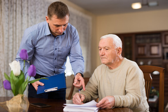 Adult man helping his senior father filling out financial documents at home
