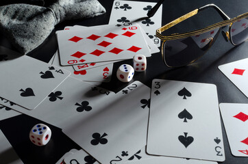 Closeup of playing card, dices, glasses, bow tie on the black desk.Concept of poker club