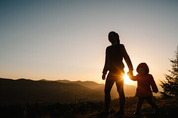 Silhouette mother and daughter, enjoying time together, walking on sunset on top of foggy mountain. Tourists on background autumn nature. Hikers on sunlight in trip in country Europe. Happy family.