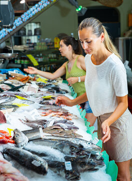 Female customers choosing fresh raw seafoods from large assortment of fish store
