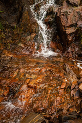 Small creek with water fall flows through very orange stones. Nature background.