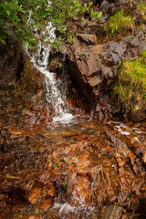 Small creek with water fall flows through very orange stones. Nature background.