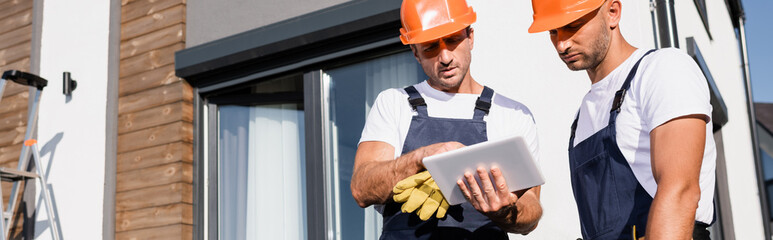 Horizontal image of workmen in hardhats and uniform using digital tablet near house