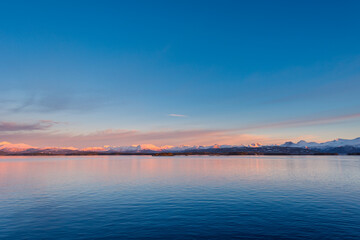 Fototapeta na wymiar Panoramic vista of the coast of Norway with snow covered mountains in beautiful soft evening light