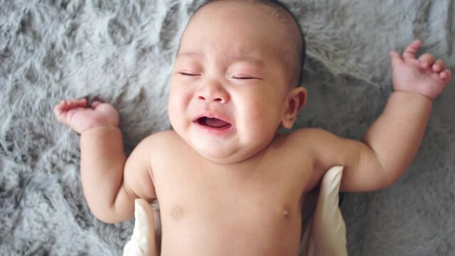 HD slow motion, Hand lift up babe crying, Asian baby lying cry on grey carpet.