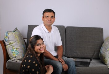 young Indian couple using the laptop sitting on a sofa.