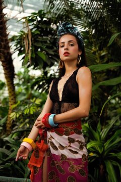 Tropical garden. A beautiful brunette with a golden tan poses in floral headdress in green leaves. Face with clean skin, red lips.