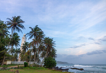 Fototapeta na wymiar Historic stone lighthouse in Sri Lanka, flanked with coconut palm trees. 