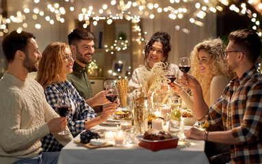 holidays, celebration and people concept - happy friends having christmas dinner at home drinking non-alcoholic red wine
