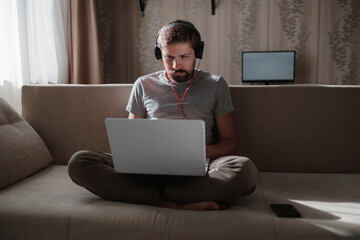 Man on sofa with headphones and notebook at home