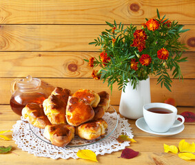 Beautiful autumn still life with a bouquet of marigolds and appetizing potato pies in the form of fallen leaves on a lace napkin and a cup of tea on a wooden background