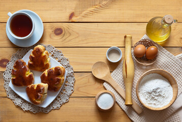Ingredients for kneading homemade dough: flour, dry yeast, eggs, sugar and seed oil. Appetizing freshly baked potato pies and cup of tea on wooden background. Flat lay, copy space, top view, close-up