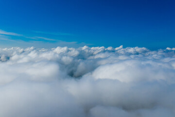 White clouds. View from the window of an airplane. Clouds below and blue sky above.