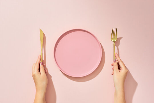 Woman with fork, knife and empty plate on pink background, top view