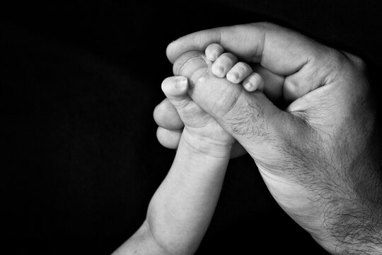 mano de bebé sosteniendo mano de adulto en blanco y negro
