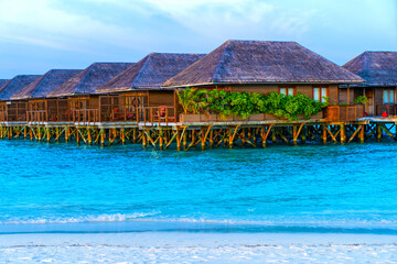 Wooden bridges leading to the huts on the shores of the tropical, warm sea. Maldives. Tourism concept.