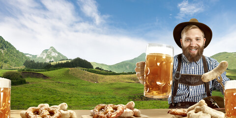 Fototapeta premium The happy smiling man with beer dressed in traditional Austrian or Bavarian costume holding mug of beer, mountains on background, flyer ready for ad. The celebration, oktoberfest, festival concept.