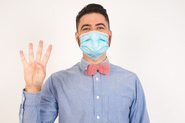 Young man standing against gray wall showing and pointing up with fingers number four while smiling confident and happy.