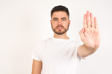 Obraz premium Young handsome caucasian man doing stop gesture with palm of the hand. Warning expression with negative and serious gesture on the face isolated over gray background.