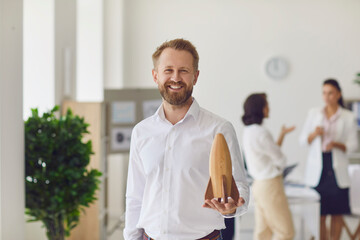 Happy smiling business owner looking at camera and holding wooden rocket as symbol of new start-up - obrazy, fototapety, plakaty