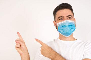Advertisement concept. Positive, pretty, caucasian man with beaming smile in shirt on grey background is pointing with his two index finger and looking on empty copy space.