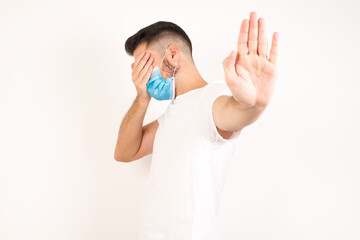 People, body language. Young European man covers eyes with palm and doing stop gesture, tries to hide from everybody. Don't look at me, I don't want to see, feels ashamed or scared.