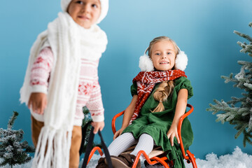 selective focus of kid sitting on sleigh near boy in winter outfit on blue