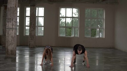 Man and woman with dreadlocks in fitness studio doing exercises together, performing push ups with jumps and claps. Loft interior. Front view