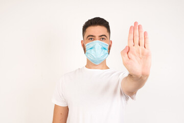 Handsome Caucasian man wearing medical mask and doing stop gesture with the palm of the hand. Protection against infectious disease concept.