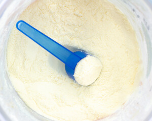 Dairy or milk powder in a container with a blue plastic spoons for children is formula as a baby food or as a health supplement