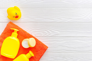 Bath accessories for kids. Yellow rubber duck,towel, cream, shampoo on white wooden background top view