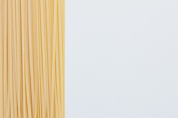Bunch of raw linguine pasta on left side of white background, copy space
