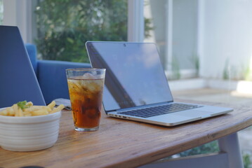 A refreshing glass of iced tea with ice cubes sits on a wooden table, partially in focus, suggesting a break during work or study. 