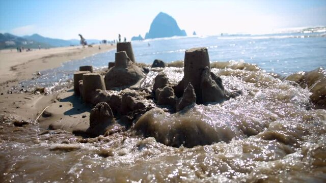 Waves crashing over sandcastle on the beach. Sandcastle being destroyed by waves. (slow motion)