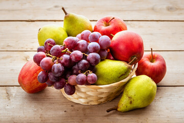 Ripe fruits apples, pears and grapes in a wicker basket on a wooden table.