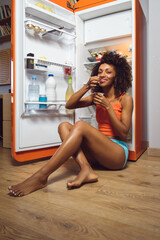 Fototapeta na wymiar Beautiful slim black woman eating yogurt at home at night. Fit afro hairstyle female taking healthy snack.