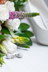 Obraz na płótnie Canvas Wedding accessories. Pearl earrings with diamonds, white shoes and a bridal bouquet with white roses on a light background.