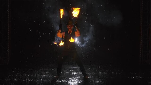 Silhouette of a man doing a professional fire show in a dark studio in the rain. Slow motion.