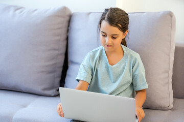 Naklejka premium Cute little girl using laptop at home. Education, online study, home studying, distance learning, schoolgirl children lifestyle concept