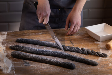 Chef preparing and cutting the dough for cooking black dumplings with sepia addition on the wooden table. Cooking dumplings – step by step guide.