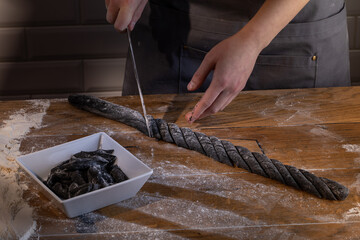 Chef preparing and cutting the dough for cooking black dumplings with sepia addition on the wooden table. Cooking dumplings – step by step guide.