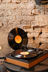 Close up of old vinyl player and vinyl records on a table in front of a brick wall.