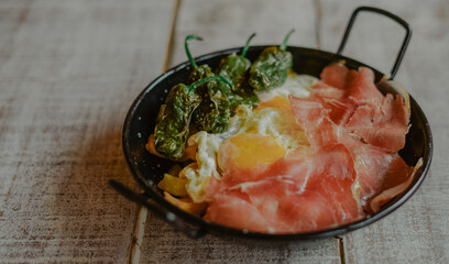 Delicious spanish tapa consisting of a frying pan with eggs, ham,  green peppers and fried potatoes