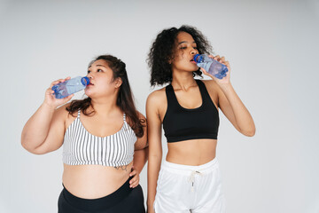 Asian chubby and african women drinking water from bottle at white background.