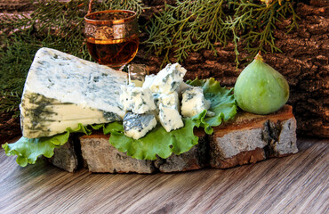 Slices of blue cheese on a green lettuce leaf with figs on a background of tree bark. A shot of alcohol