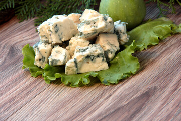 Cheese with mold on a green lettuce leaf with figs on a wooden background.