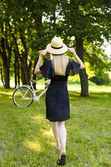 A girl in a summer dress and hat walks in the summer in the park.