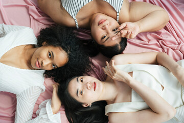 Flat lay - African and thai women in white dress laying on pink background.